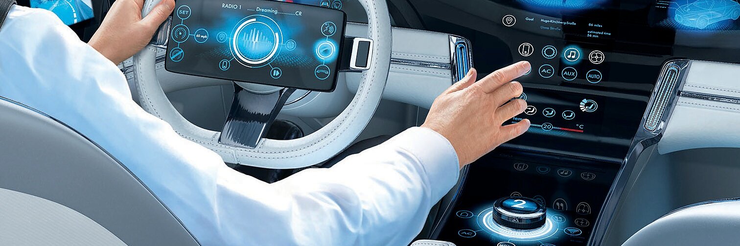 A person in a white jacket operates a futuristic car with digital displays and touch controls. The dashboard shows various electronic interfaces. The view outside suggests a cityscape with modern buildings. All exposed wiring within the vehicle has been neatly secured using tesa tape, ensuring a clean and organized appearance. (This text has been generated by AI)