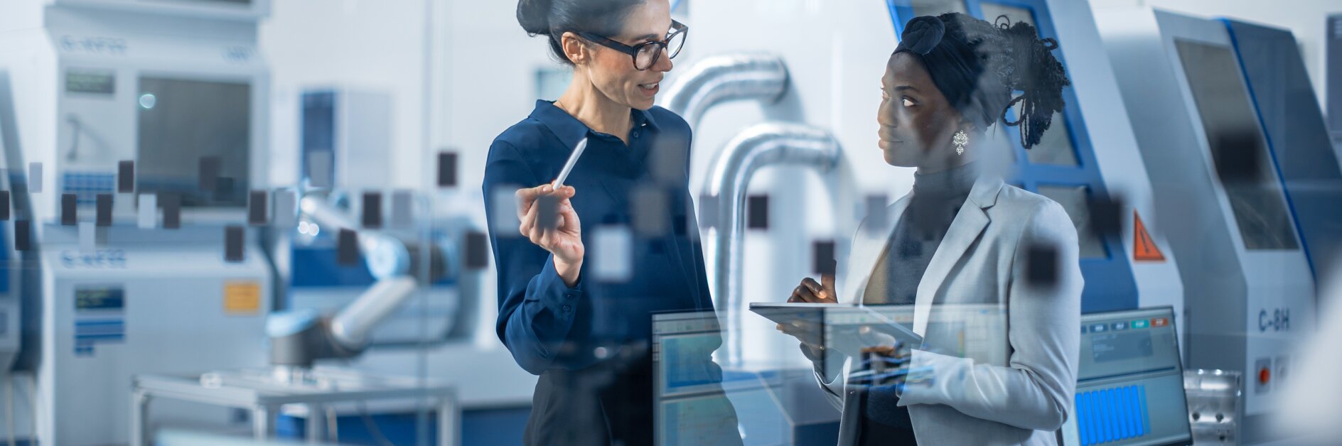 工業工程師與項目主管交談，他們使用數字平板電腦討論現代工廠規劃。配備數控機床和機械臂裝配線的生產設施