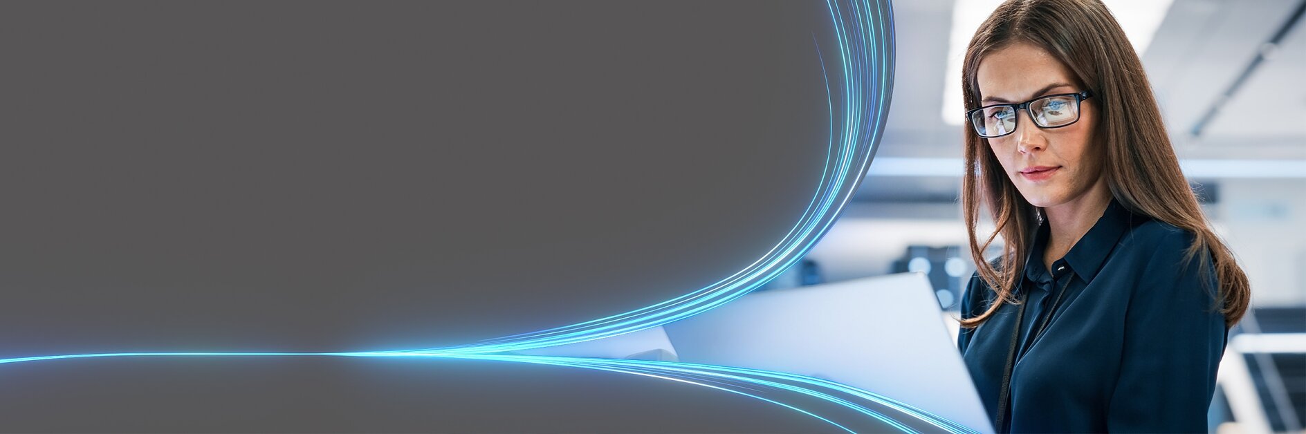 A woman with long brown hair and glasses is looking at an open laptop. She is in a modern, brightly lit office setting. Blue curved light trails are seen on the left side of the image, creating a dynamic visual effect. (This text has been generated by AI)